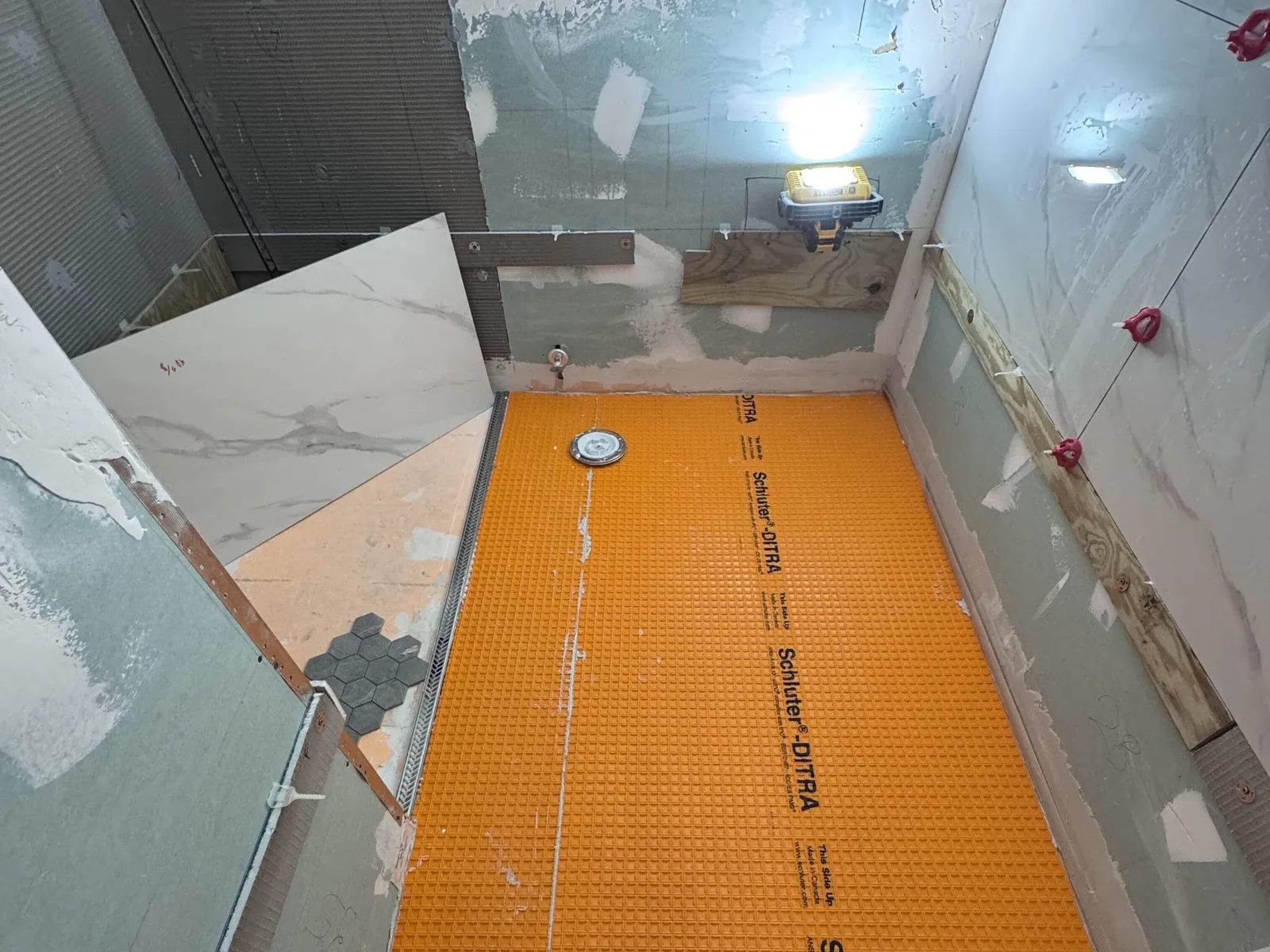 Shower floor covered with an orange waterproofing membrane around a linear drain, with mosaic floor tile and a large tile panel ready to set