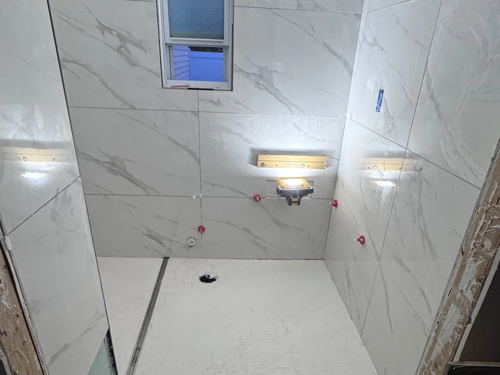 Window inside a tiled shower with wall sconces and marble-look porcelain walls in a St. Petersburg bathroom remodel
