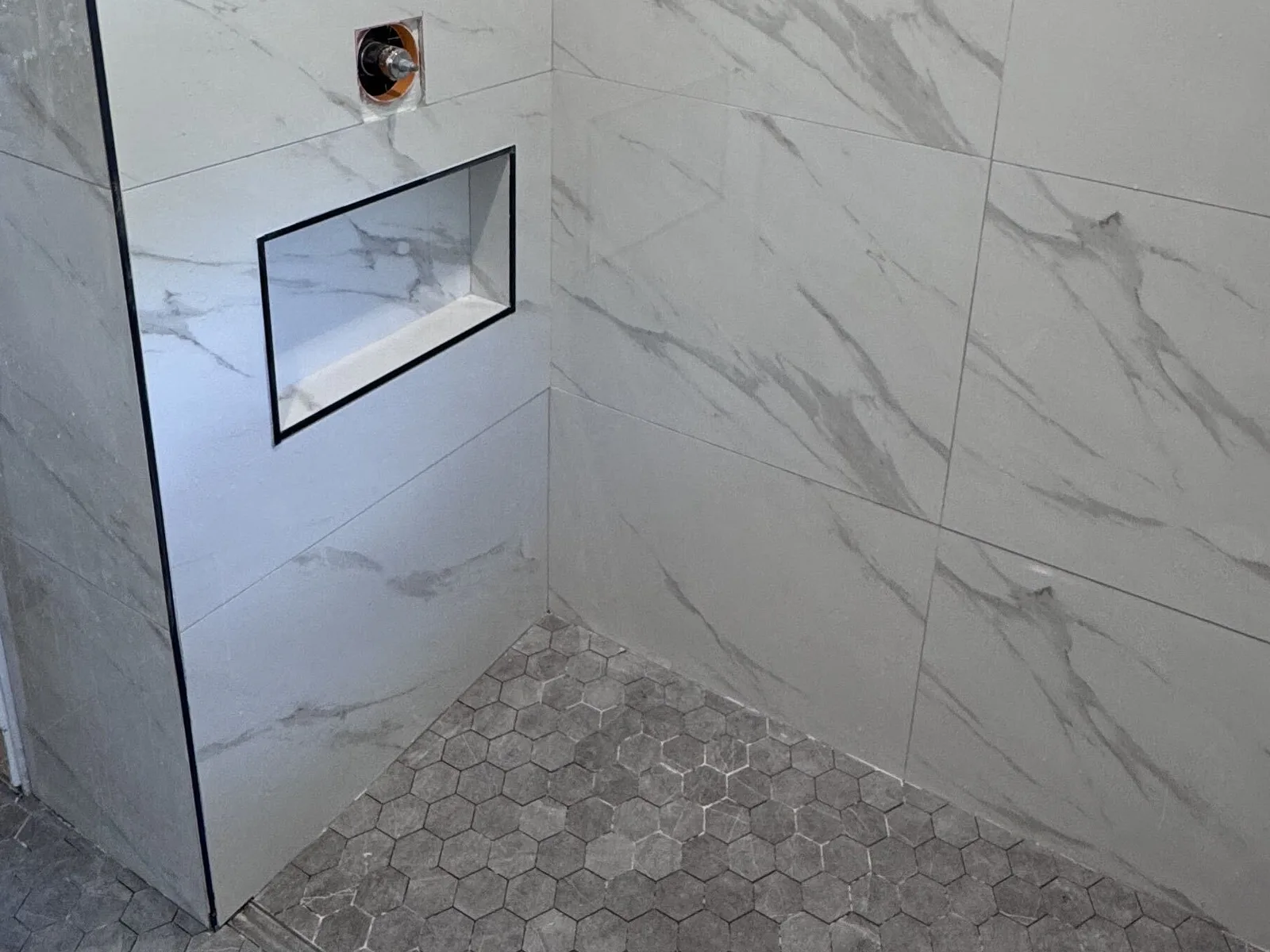 Close-up of a tiled shower niche and shower valve set into large-format marble-look porcelain in a St. Petersburg bathroom remodel