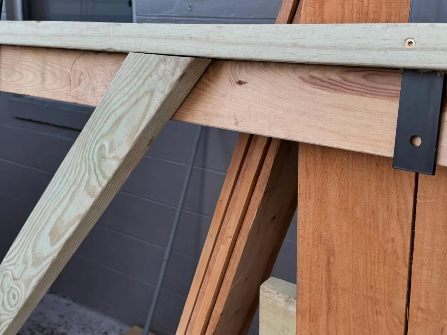 Close-up of a gate frame's pressure-treated brace and rail joined to cedar boards with a black steel bracket