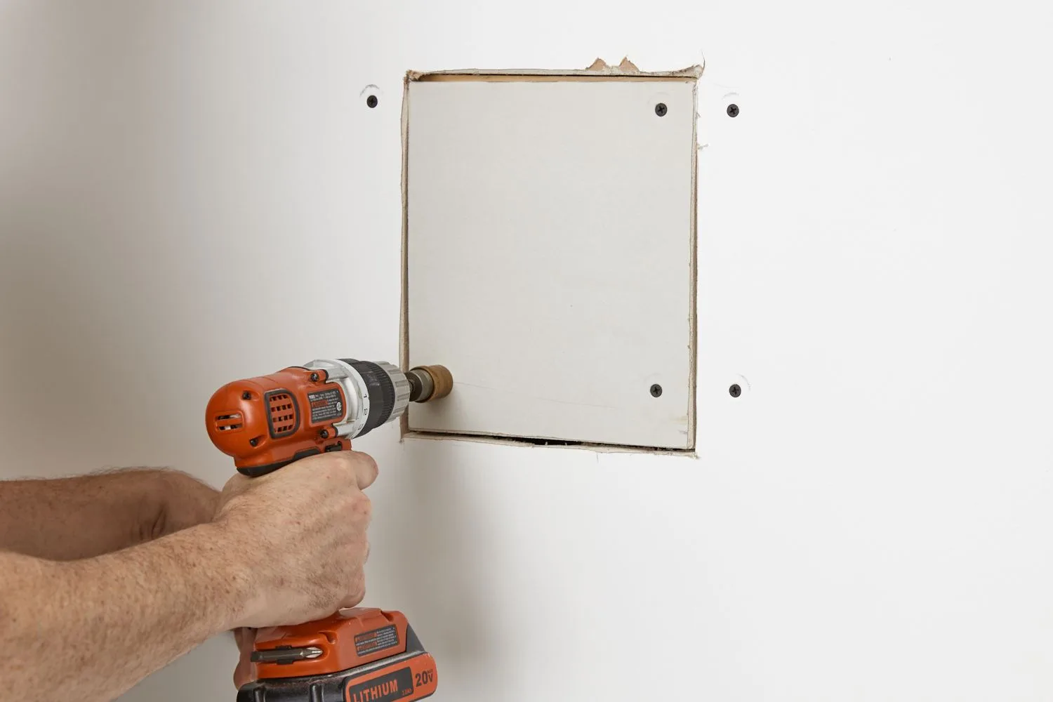 Drill driving screws into a cut-in drywall patch over a hole in a wall