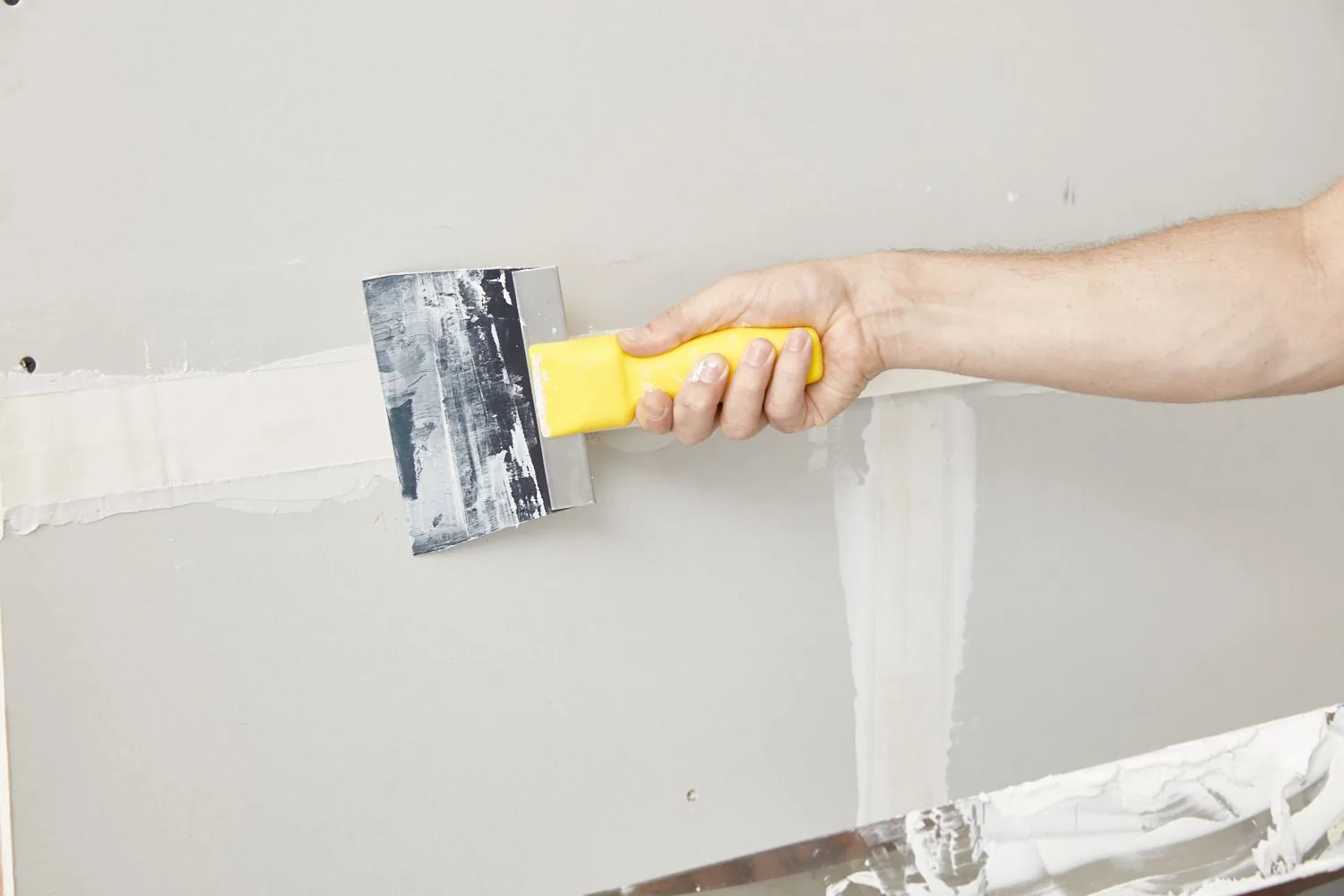 Taping knife spreading joint compound over a drywall seam next to a mud pan