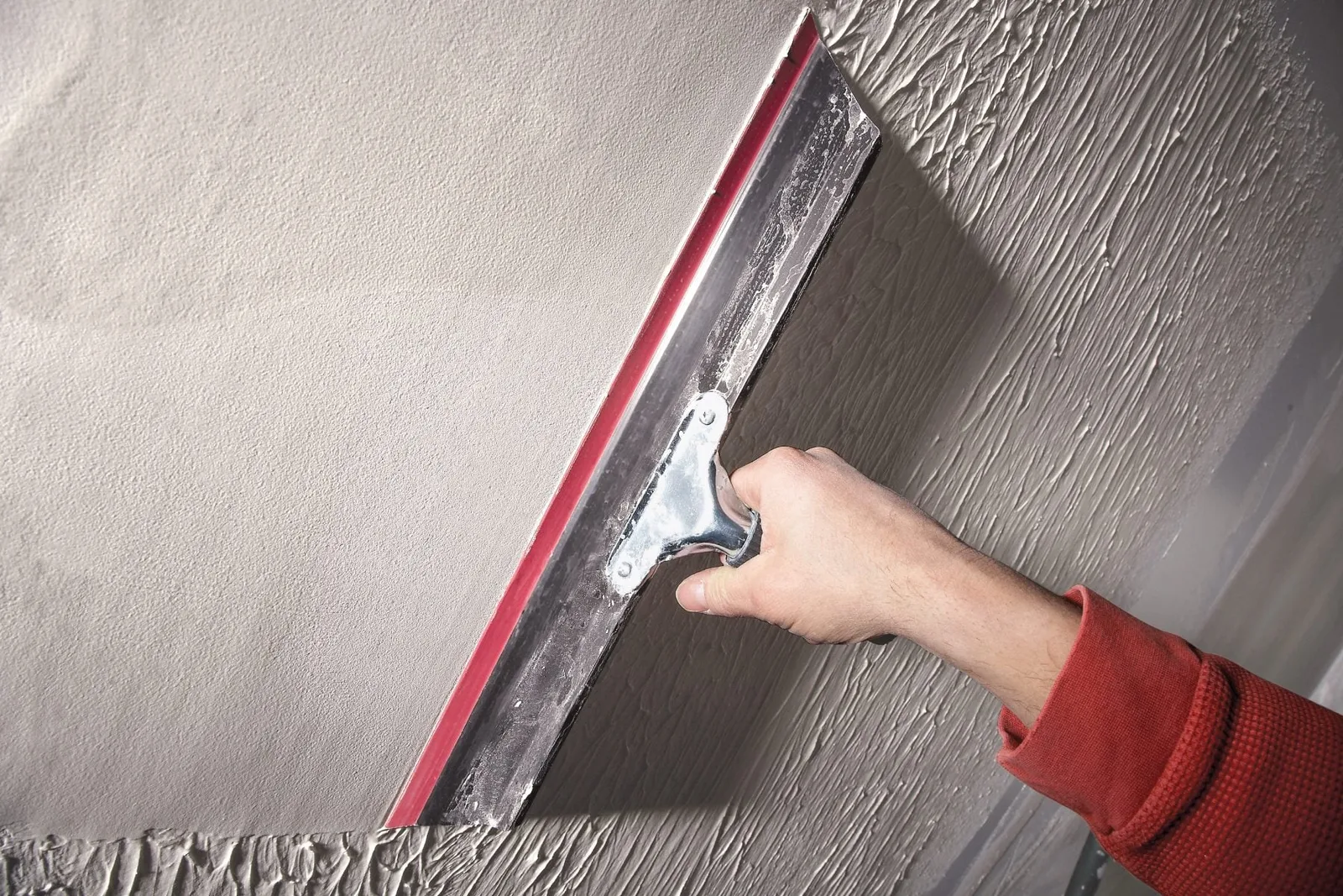 Wide taping knife skimming joint compound across a textured wall to blend it smooth