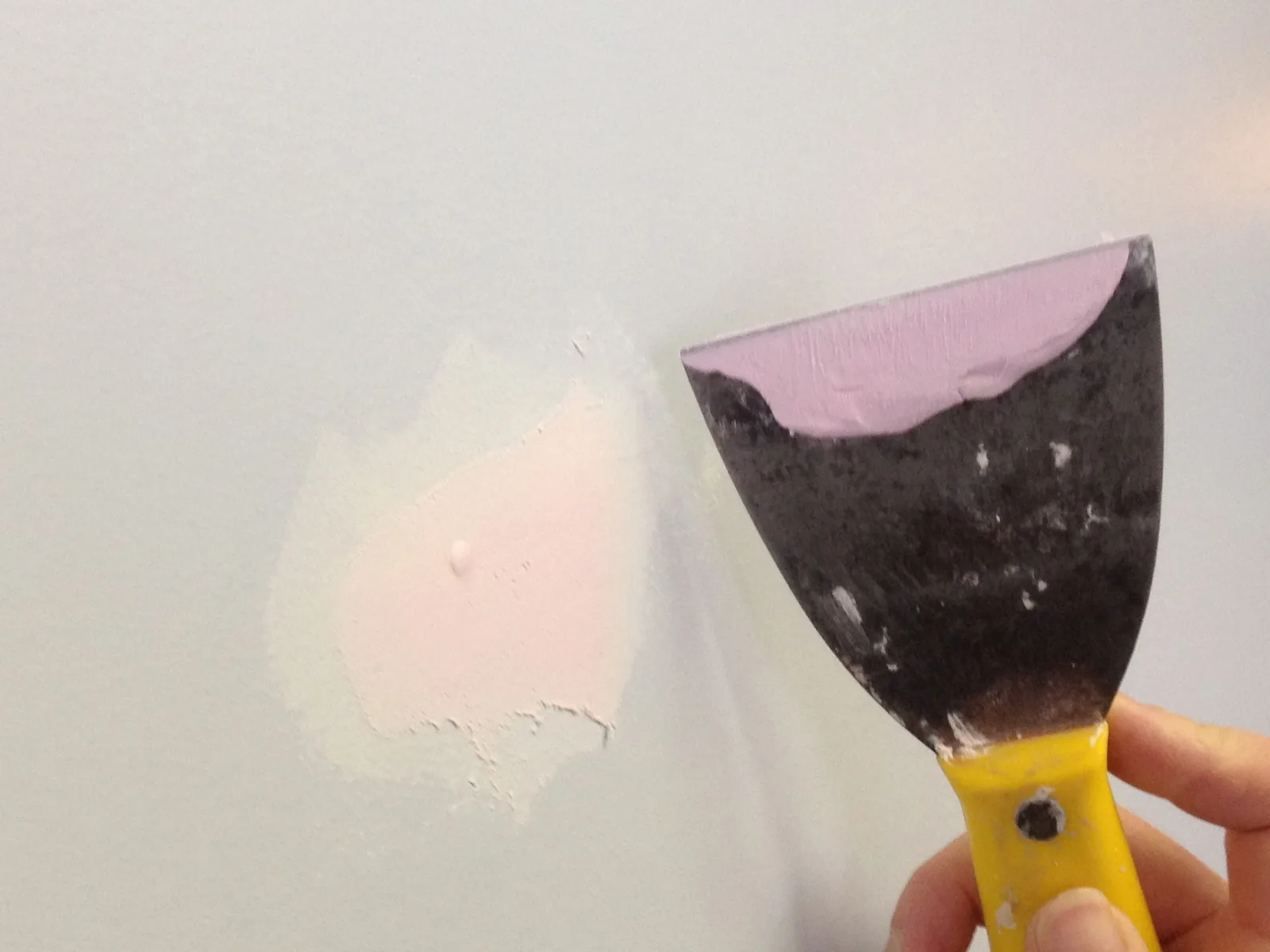 Putty knife smoothing spackle over a small patched hole in a painted wall