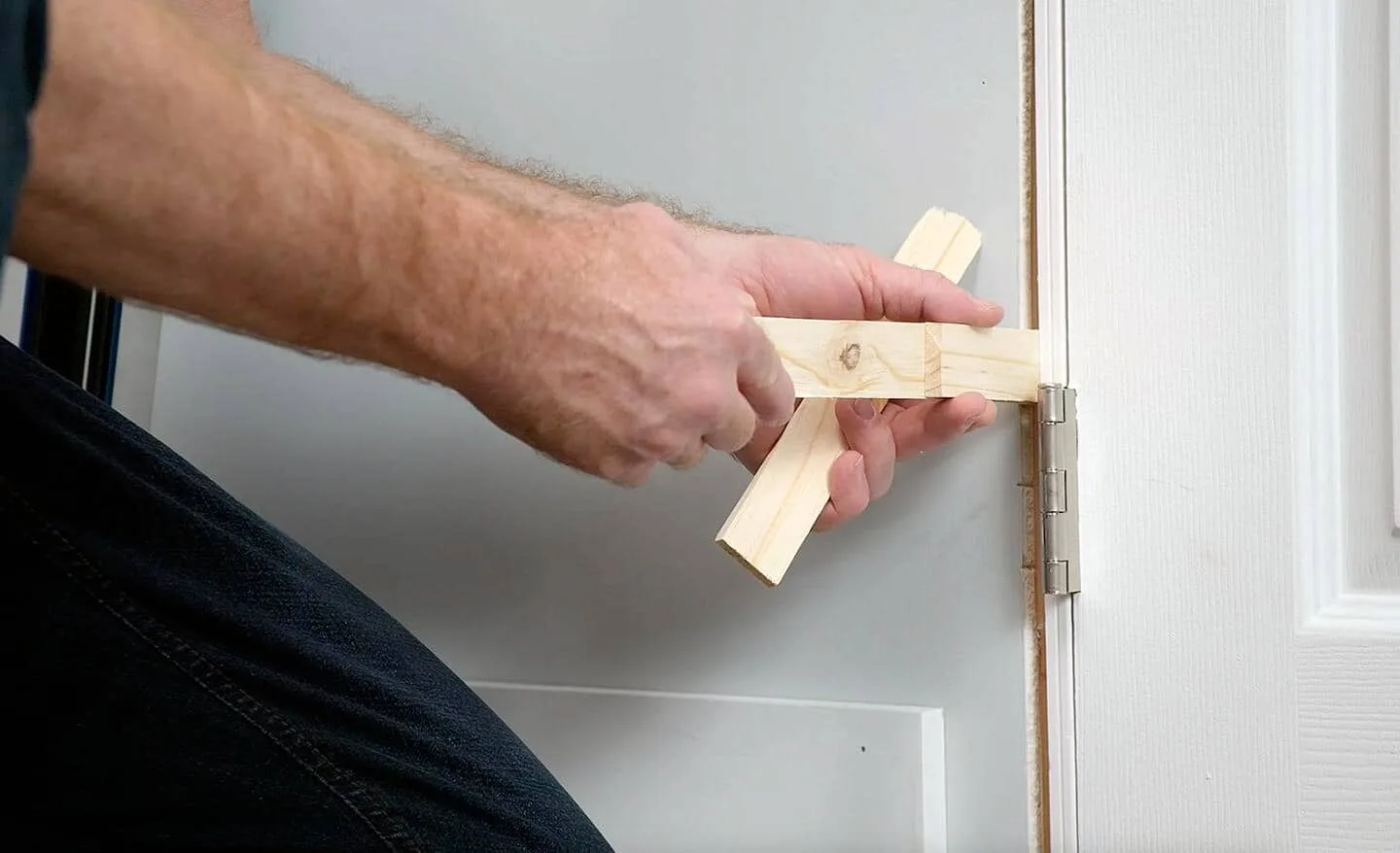 Hands setting wood shims behind a door jamb at the hinge while hanging an interior door