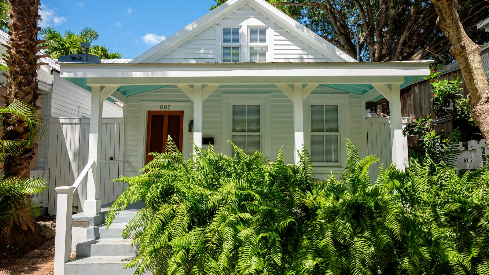 White Florida bungalow with a covered front porch, ferns and a palm in the front yard