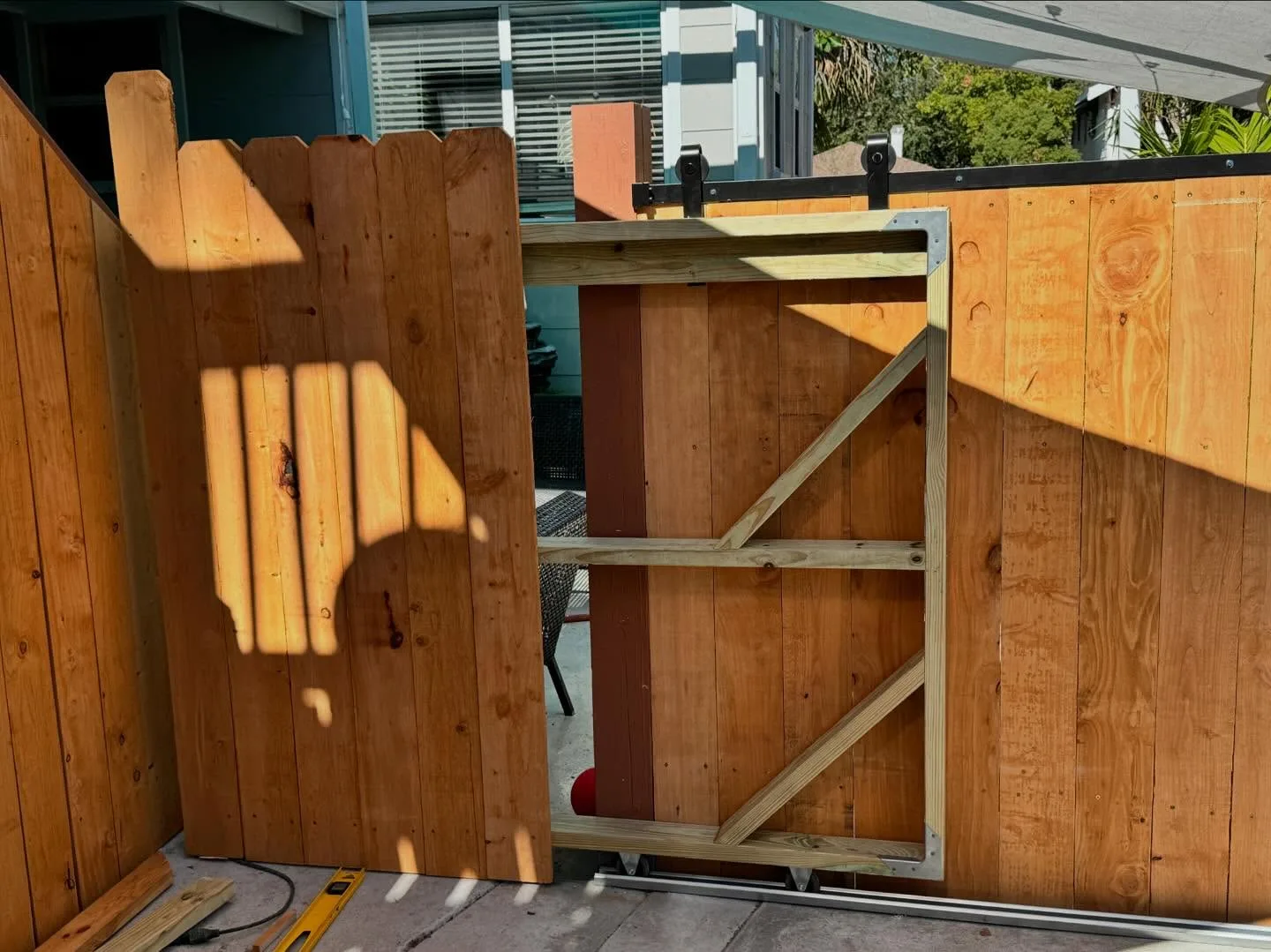 Sliding wood gate hung from a black top-mounted track with roller brackets beside a cedar privacy fence