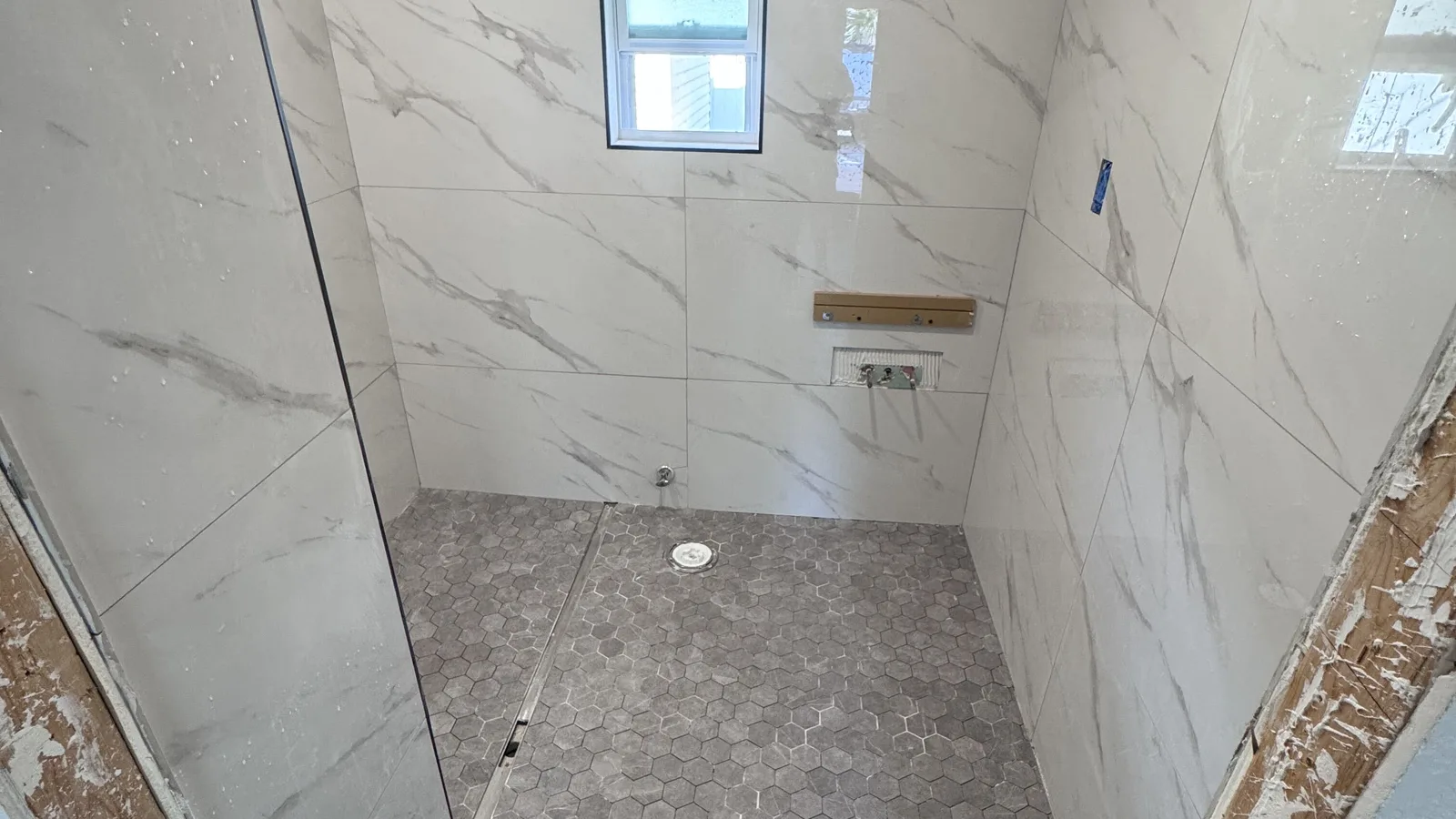 Walk-in tile shower with marble-look walls, a grey hexagon mosaic floor, a linear drain and a window, mid-remodel in a St. Petersburg home